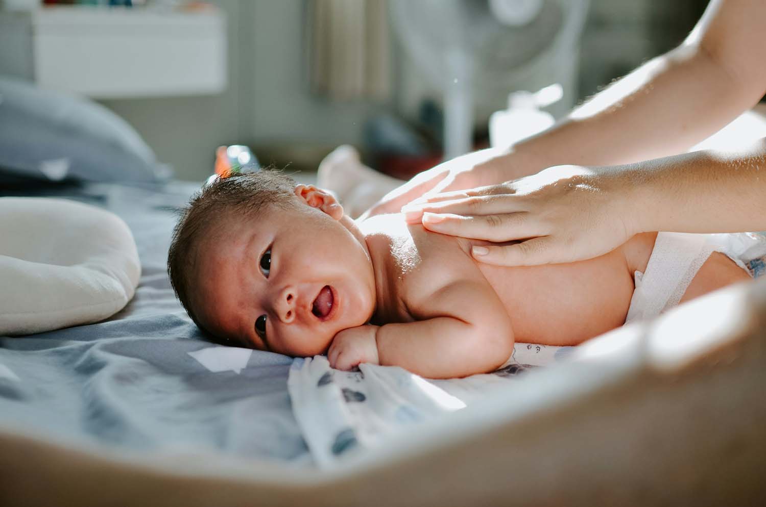 A person presses their hands against the back of a newborn child.