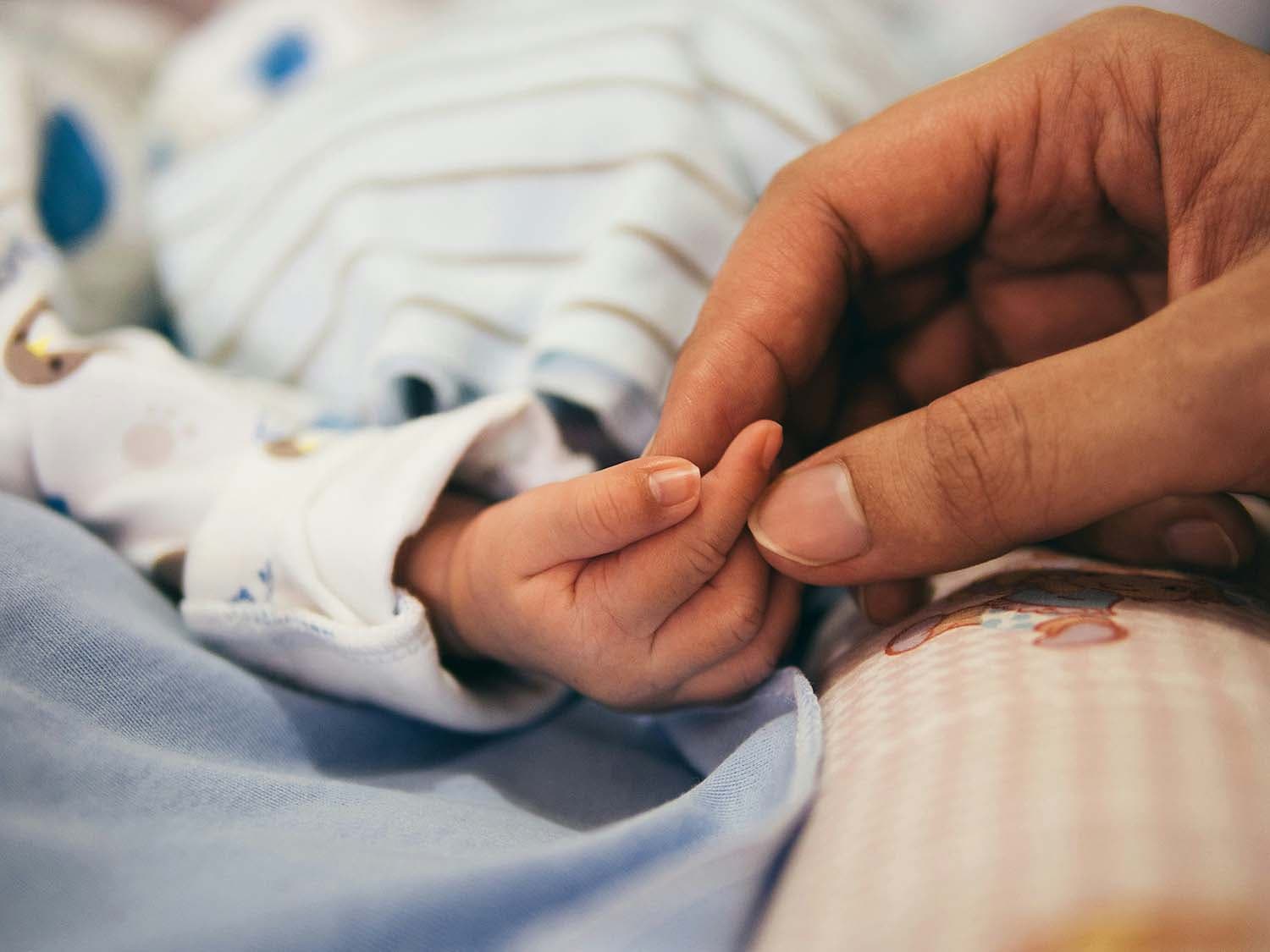 A close-up of a parent holding their infant's hand.