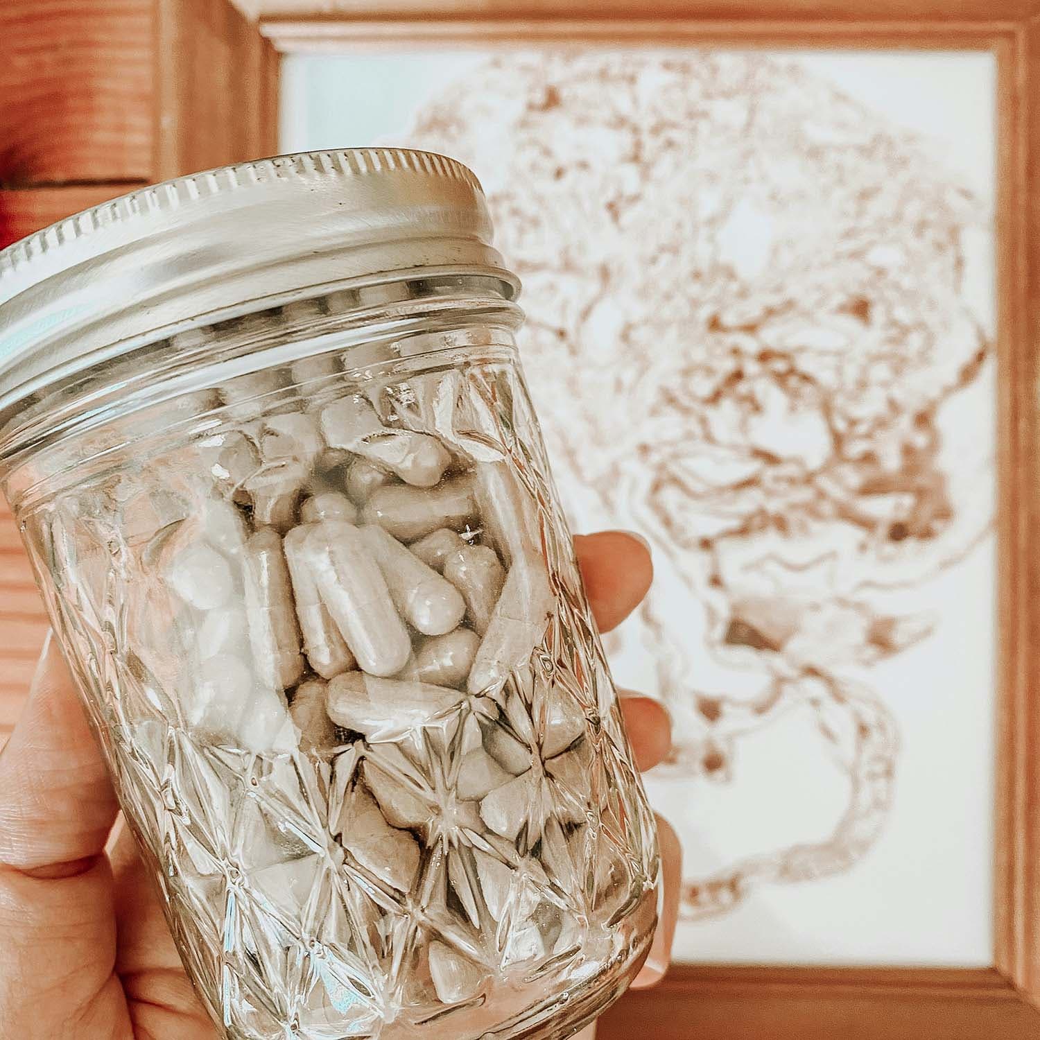 A glass jar of capsules containing a gray powder.