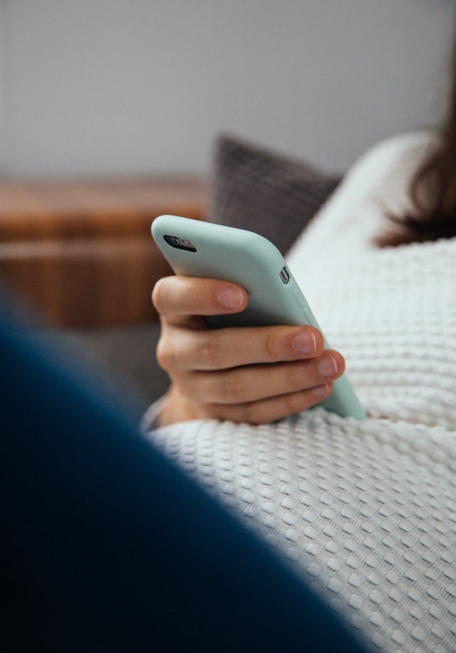 A pregnant woman browses her phone while reclining.