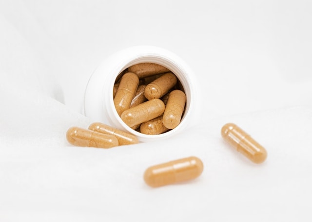 An open pill bottle with clear, powder-filled capsules spilling out.