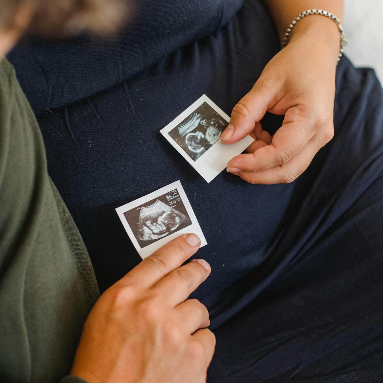 A couple holds ultrasound photos against the woman's pregnancy bump.