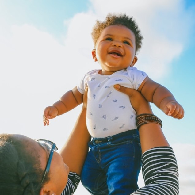 A womaon holds her child up against a bright blue sky.