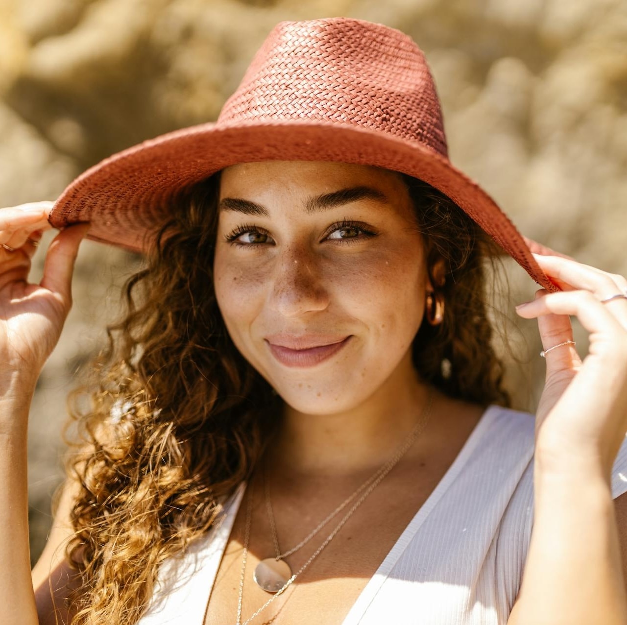 A woman smiles and tips down the edges of her pink sun hat.