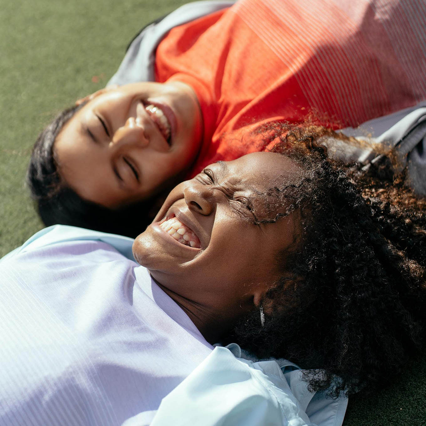 Two young women laugh while laying in the grass.